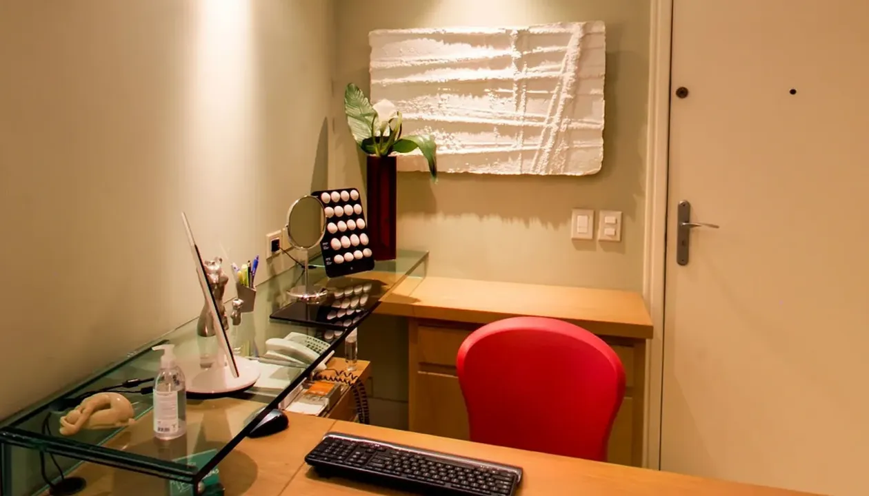 Mesa do consultório do Dr. Afrânio, com tampo de vidro, espelho de mesa e cadeira vermelha